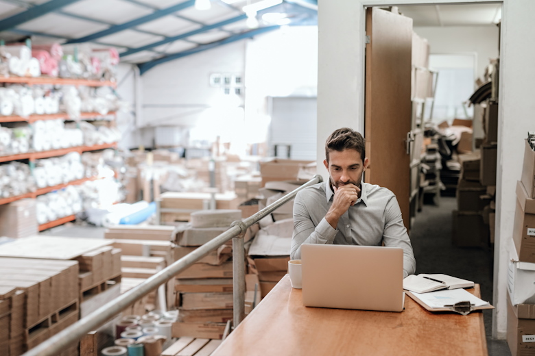 Mannelijke ondernemer achter laptop in logistieke omgeving