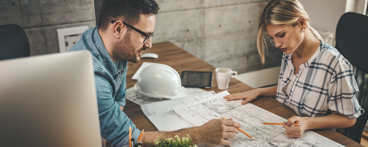 mannelijke en vrouwelijke architect aan tafel werkend aan bouwtekeningen