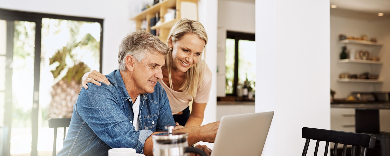 Ouder koppel die samen naar een laptopscherm kijken in hun keuken